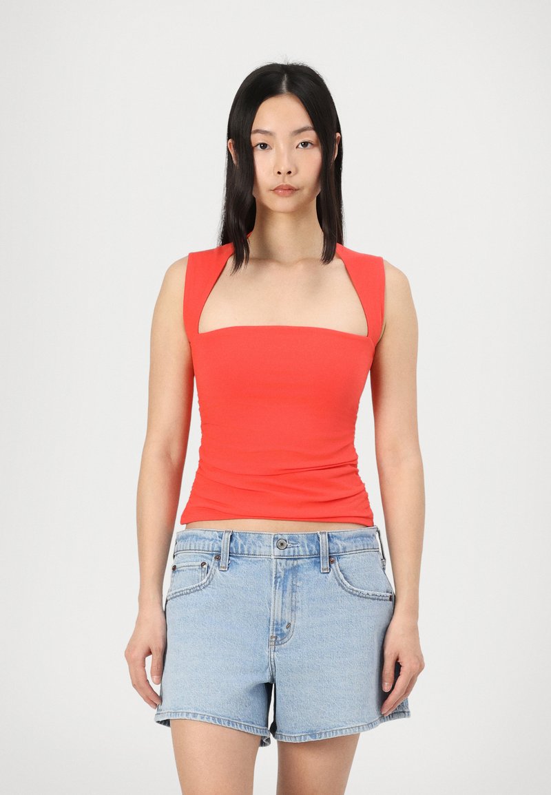 Top sin mangas rojo ajustado con escote cuadrado y tirantes anchos, combinado con pantalones cortos de mezclilla azul claro con un diseño clásico de cinco bolsillos.
