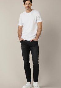 Biała koszulka z krótkim rękawem, czarne jeansy slim fit i białe trampki. Prosty design o swobodnym wyglądzie, gładka tekstura, bez wzorów.