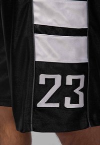 Shorts de sport noirs avec des rayures blanches sur les côtés et un grand numéro "23" brodé en noir avec un contour blanc sur la jambe inférieure.