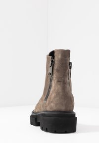 Bottine en suède taupe avec une semelle en caoutchouc noire épaisse et des doubles zips latéraux pour un enfilage facile. Fini lisse avec des détails de couture minimaux.