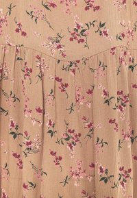 Kukkakuosisessa mekossa on vaaleanbeige kangas, jossa on vaaleanpunaisia ja vihreitä kukkia. Mekossa on kerrostettuja laskoksia ja pehmeä rakenne. Kukkakuosi on hyvin näkyvä.