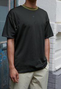 Camiseta negra de manga corta hecha de un material texturizado con un cuello verde y un sutil logo de Nike en el pecho. Combinada con pantalones de color claro.