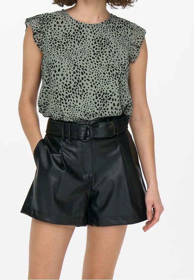 Femme portant un haut sans manches gris avec des taches noires et un short en cuir noir taille haute avec ceinture et poches.
