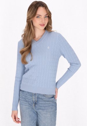 Maglione lavorato a maglia azzurro chiaro con scollo a V, texture a coste e un piccolo dettaglio di ancora bianca sul petto. Abbinato a jeans azzurri chiari.