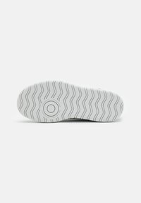 White sneaker sole with wavy tread pattern and circular logo, featuring textured rubber material for grip and durability.