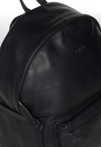 Svart läderryggsäck med rundad form, slät textur, synliga sömmar och en framficka med dragkedja.