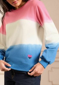 Felpa con cappuccio a maniche lunghe con un design a gradiente: colori rosa, bianco e blu. Presenta un ricamo di un piccolo cuore in rosa e nero vicino all'orlo.