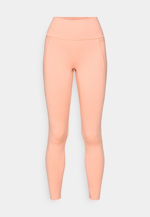 Legginsy w kolorze brzoskwiniowym wykonane z elastycznego materiału, z wysokim stanem, gładką teksturą i bezszwowym wykończeniem, bez widocznych kieszeni.