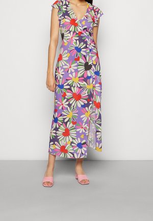 Femme portant une robe portefeuille violette avec un grand motif de fleurs multicolores et de cœurs, associée à des sandales à talon bloc ouvertes à l’avant de couleur rose.
