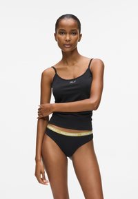 Fekete trikó vékony pántokkal, kis fehér logóval; fekete bikini alsóval, sárga, "KARL LAGERFELD" feliratos szegéllyel párosítva.