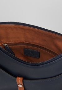 Námořnická kožená kabelka se zipovým uzávěrem, uvnitř s hnědou textilní podšívkou a vnitřní kapsou na zip. Ozdobena hnědými detaily na popruhu.