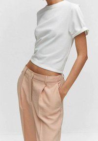 T-shirt blanc court avec manches retroussées associé à un pantalon taille haute rose pâle avec plis et poche latérale.