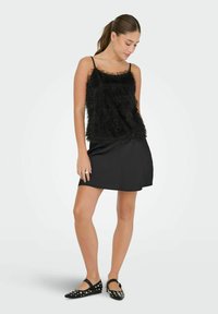 Débardeur noir en tissu duveteux avec de fines bretelles, associé à une jupe noire simple en ligne A, complété par des ballerines noires ornées de clous blancs.