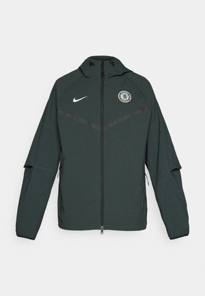 Zelená bunda Nike se zipem, kapucí a logem Chelsea FC. Má kontrastní černé akcenty a dlouhé rukávy. Vyrobena z lehkého materiálu.