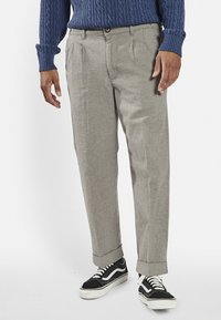 Light gray, pleated trousers with a relaxed fit, cuffed hems, and front pockets, styled with a blue textured sweater and black sneakers.