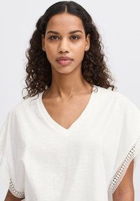 White V-neck top with short sleeves, featuring delicate lace trim along the edges. Soft, lightweight fabric with a relaxed fit.