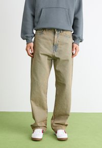 Hell gefärbte, lockere Jeans mit geradem Schnitt, die eine ausgewaschene Textur und dezente Details an den Nähten aufweisen, kombiniert mit weißen Turnschuhen.