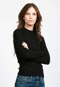 Maglione nero a coste con maniche lunghe, dal design aderente e colletto alto. Indossato con jeans denim blu con chiusura a bottone e stile a cinque tasche.