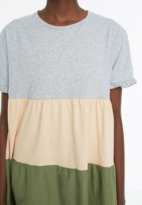 Robe t-shirt avec un haut gris, un milieu pêche et un bas vert olive. Fabriquée en tissu doux avec des manches courtes volantées et une coupe décontractée.