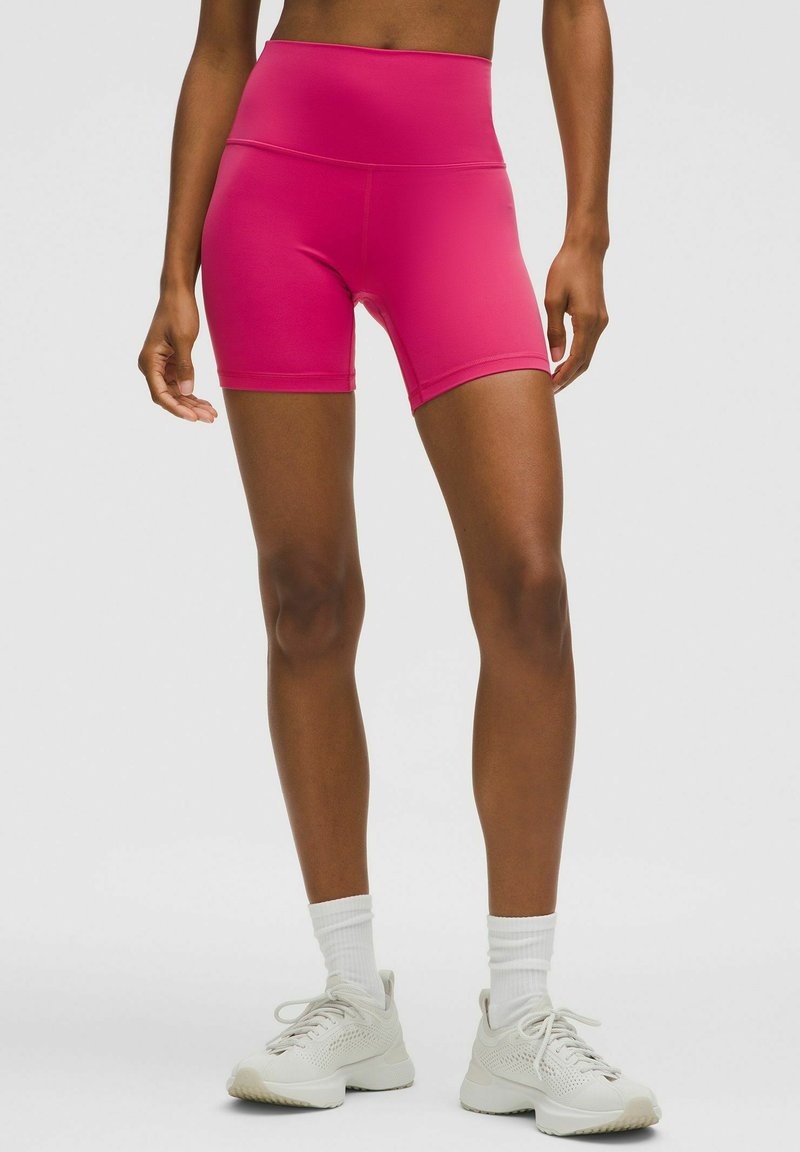 Shorts ajustés taille haute en tissu extensible de couleur rose, avec une texture lisse et une coupe mi-cuisse.