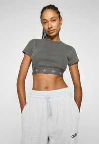 Šedý žebrovaný crop top s krátkými rukávy a tónovaným logem. Kombinován se světlými šedými tepláky s nastavitelným páskem.