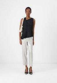 Svart peplum-topp, sølvfargede, skinnende skreddersydde bukser, svarte høye hæler og en lys grå håndveske. Strømlinjeformet design med moderne silhuett.