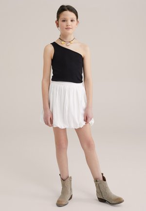 Top nero a una spalla, gonna bianca fluida con vita elastica e stivaletti beige alla caviglia. Accessoriata con una collana floreale colorata.