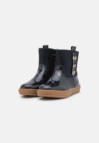 Bottines en cuir verni bleu marine avec une finition lisse, bout rond et semelle en caoutchouc. Présente des accents de boucle décoratifs sur le côté.