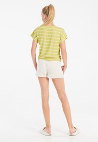 Top a maniche corte a righe verde lime abbinato a pantaloni corti color crema. Il top presenta una vestibilità rilassata e i pantaloni corti hanno una consistenza morbida.