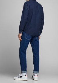 Camisa de manga larga azul marino con cierres de botones, combinada con jeans azul oscuro de corte entallado. Atuendo completado con zapatillas blancas con detalles en negro.