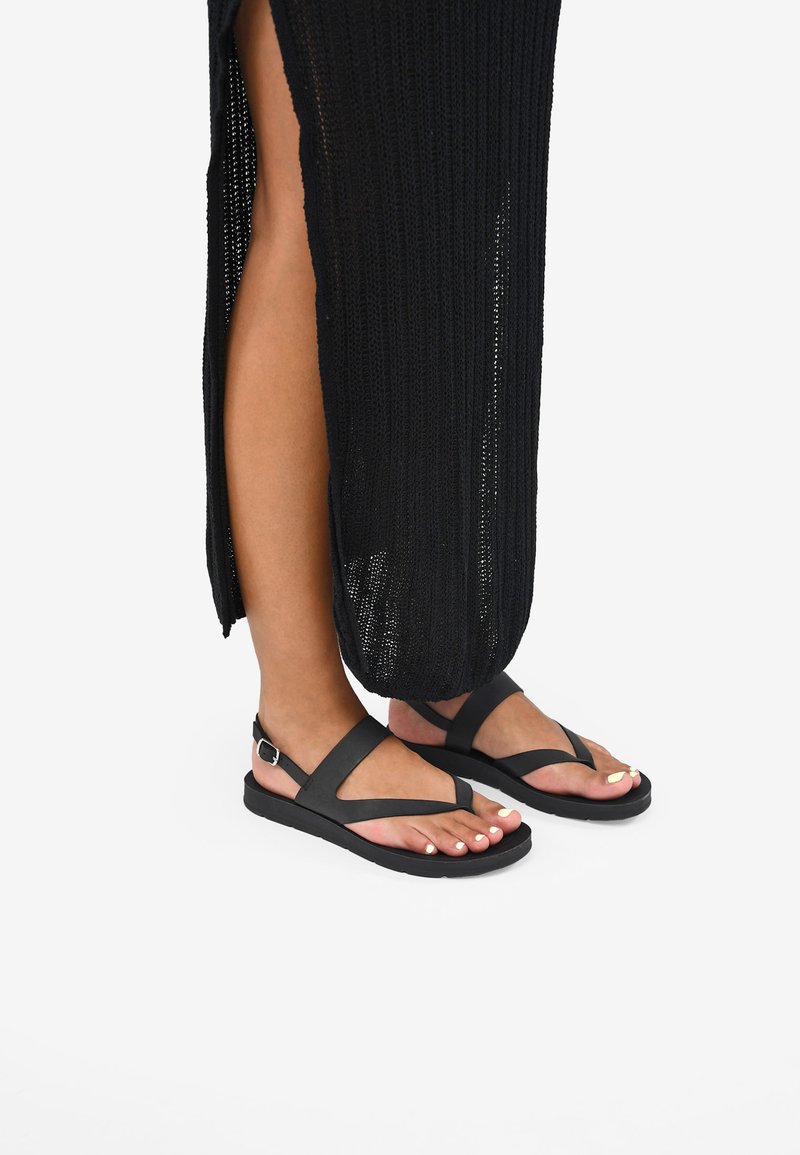 Sandali piatti neri con un design semplice, caratterizzati da strap incrociati e una fibbia. Suola in gomma e silhouette minimalista.