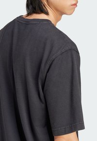 Czarny bawełniany t-shirt z krótkimi rękawami, okrągłym dekoltem i miękką teksturą. Posiada widoczne szwy i luźny krój.