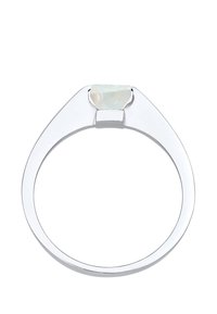 Strieborný prsteň s zužujúcim sa pásikom, s brúseným, priesvitným bielym drahokamom zasadeným v minimalistickom dizajne. Hladký, lesklý povrch.