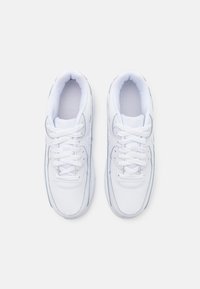 Chaussures de sport blanches avec une tige en synthétique lisse, bout rond, col rembourré et fermeture à lacets. Présente des détails subtils en gris sur les côtés.