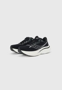 Μαύρα και λευκά παπούτσια τρεξίματος Saucony με παχιά μαξιλαρωτά πέλματα, επάνω μέρος από δίχτυ και λογότυπο στο πλάι, εμφανιζόμενα σε πλάγια μπροστινή όψη.