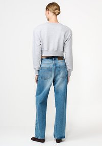 Pilkas trumpas megztinis su apvaliu iškirpimu derinamas su šviesiai mėlynomis aukštu juosmeniu džinsinėmis kelnėmis, turinčiomis nublukusį raštą ir užpakalinėmis kišenėmis.