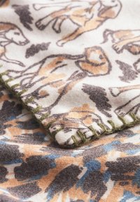 Tissu à motif mettant en vedette des éléphants stylisés en marron et beige sur un fond clair, avec des coutures visibles en accents de vert et de bleu.