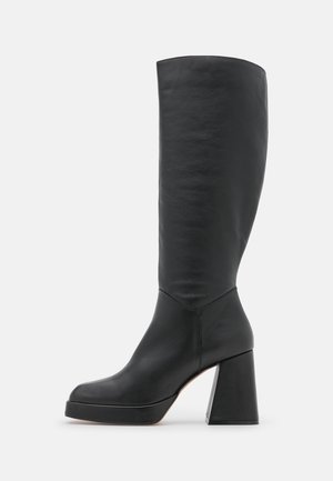 Bota negra de piel a mitad de la pantorrilla con tacón de bloque y suela plataforma, vista lateral sobre fondo blanco.