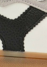 Elemento negro texturizado con una superficie blanca lisa adyacente y un acento gris, que presenta detalles cosidos y un ligero brillo.
