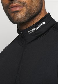 Veste zippée noire en tissu doux avec un col haut. Présente le logo "ICEPEAK" en blanc sur le col et une fermeture éclair à l'avant.
