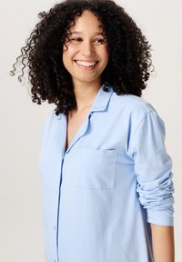 Lichtblauwe, lange mouwen shirt met een knoopsluiting en een borstzak, gemaakt van zacht materiaal; heeft opgerolde mouwen en een relaxte pasvorm.