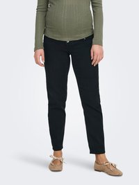 Blugi negri din denim cu croială strâmtă, având un sistem de închidere cu nasturi, și un top cu mâneci lungi, texturat, cu dungi, de culoare verde măsliniu. Balerini maro deschis cu panglică.