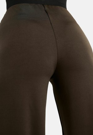 Pildivõte pruunidest kõrge vöökohaga retuusidest inimesel, näidates kangakudet ja keskmist õmblust seljal.