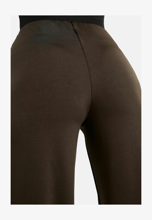 Pildivõte pruunidest kõrge vöökohaga retuusidest inimesel, näidates kangakudet ja keskmist õmblust seljal.