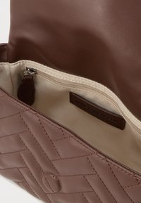 Brązowa pikowana skórzana torebka w kolorze beżowym z materiałowym wnętrzem i kieszonką na zamek, z metką Karla Lagerfelda wewnątrz.