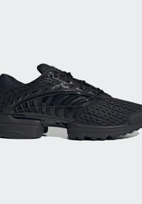 Μαύρο αθλητικό παπούτσι με δίχτυ πάνω μέρος, γυαλιστερές πλευρικές λεπτομέρειες, μαλακή σόλα και ανάγλυφη εξωτερική σόλα σε απλό φωτεινό φόντο.