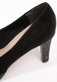 Black suede high-heeled shoe with a textured black metallic heel. Interior is beige, featuring a smooth texture.