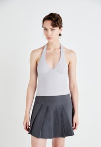 Svetle šedý halter top s hlubokým výstřihem ve tvaru V v kombinaci s tmavě šedou skládací sukní, která se vyznačuje hladkou texturou a přiléhavým pasem.