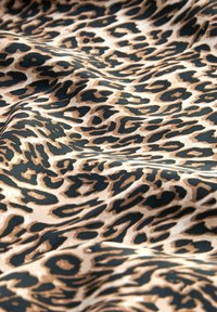 Gros plan d’un tissu avec un motif léopard ondulé en noir, marron et beige.
