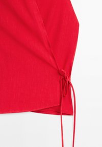 Red fabric with a side tie detail, showing a knot and long loose ends against a white background.